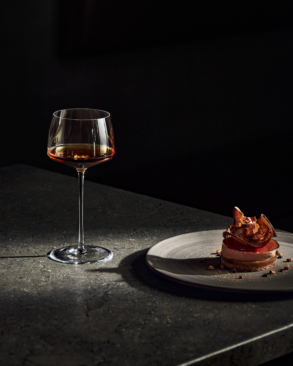 Cocktailglas steht auf einem Tisch, daneben wird ein Teller mit einem Dessert gezeigt